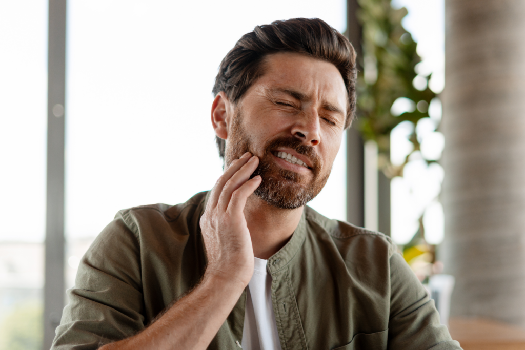 Man holding his jaw in pain due to a severe toothache or dental infection, indicating the need for urgent dental care.