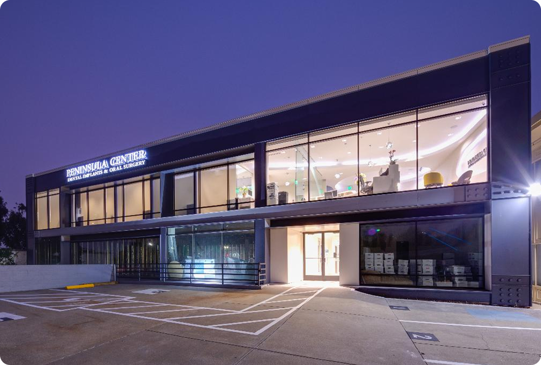 Exterior view of a modern oral and maxillofacial surgery clinic with a welcoming entrance and parking area.