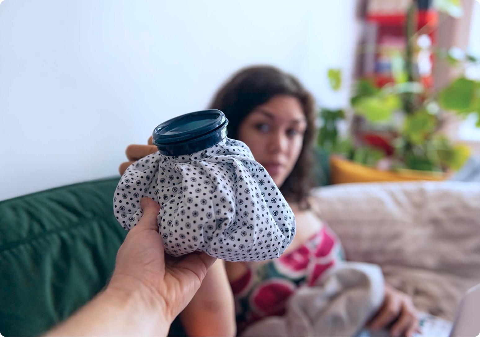 A person holds a cold compress while a child rests on a couch, representing at-home care and recovery after treatment.