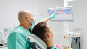 Dentist explaining a personalized treatment plan using a digital 3D dental scan displayed on a computer monitor while the patient watches.