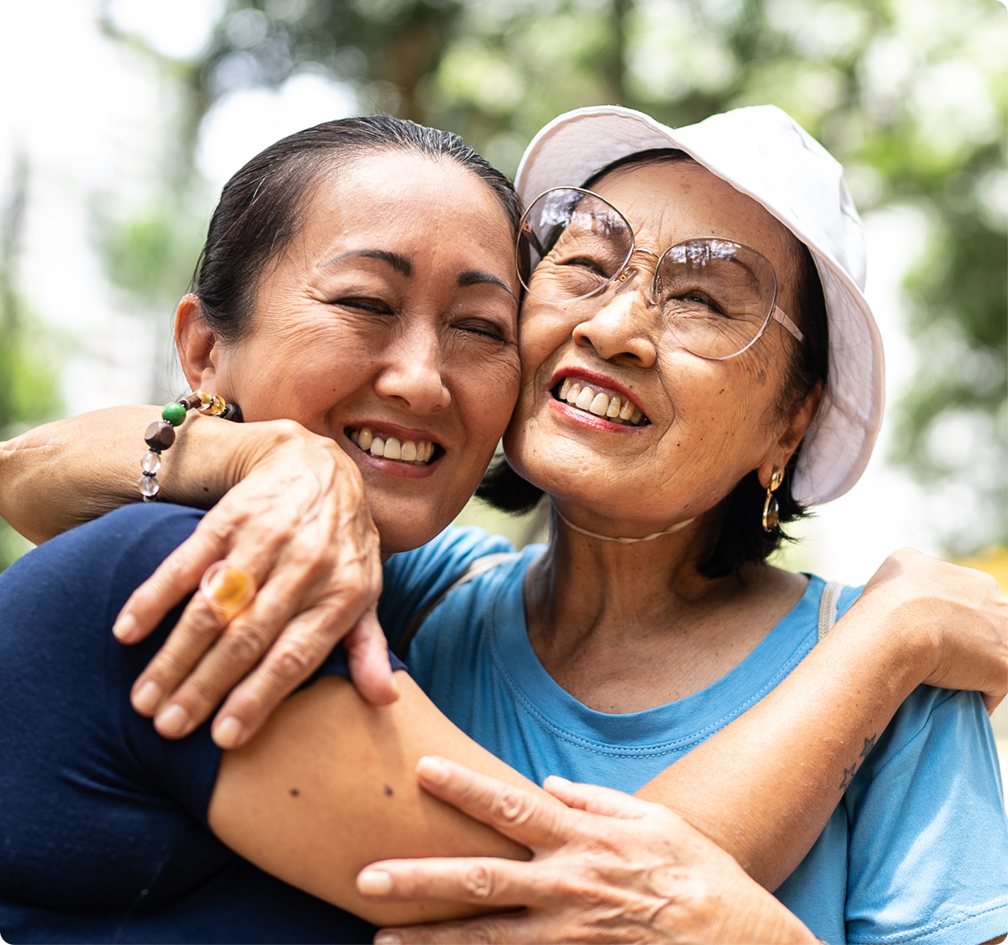 Two smiling women sharing a warm hug outdoors, representing confidence, comfort, and improved quality of life after successful dental care.